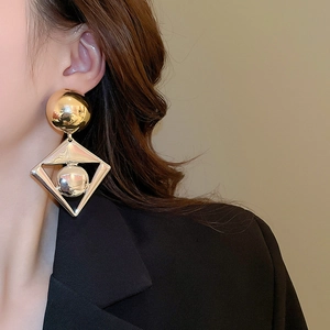 Macro view of geometric gold rhombus earrings with spheres on model in black suit