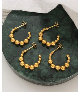 Gros plan de boucles d'oreilles créoles perlées dorées sur plateau en marbre vert