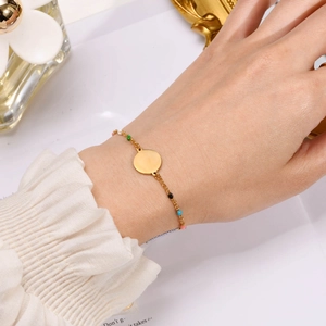 Detail of a gold bracelet with colorful enamel beads and a polished round pendant on wrist