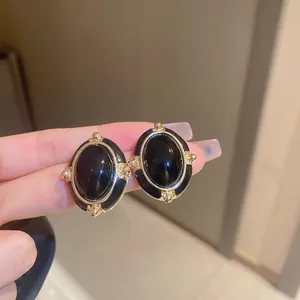 Close-up of black oval enamel earrings with gold trim and retro geometric design