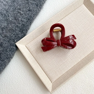 Macro detail of wine red bow hair claw clip with golden spring on a beige textured tray