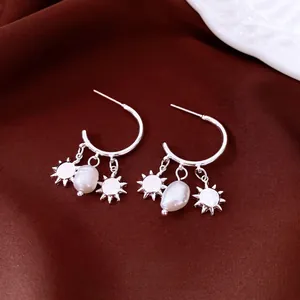 Silver needle pearl sun pendant earrings displayed on elegant dark velvet background
