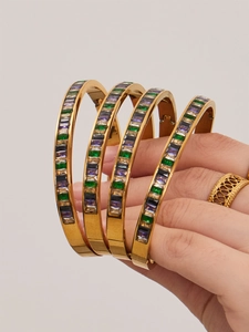 Detail of four gold-tone stainless steel bangles with colorful square cubic zirconia stones