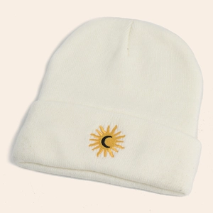 Close-up of sun and moon embroidery on a white chunky knit beanie with soft texture