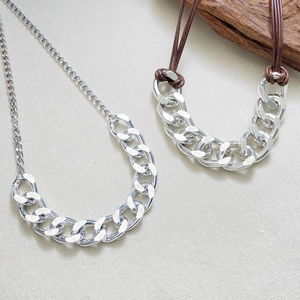 Close-up of thick silver chain necklaces with metal links and woven brown rope detail