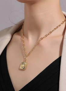 Detailed view of a gold rectangular sunburst pendant with crystal on an oval link chain