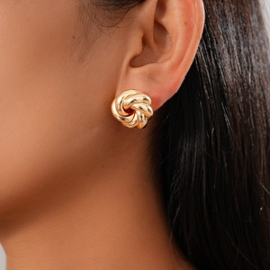 Close-up of elegant gold knot stud earrings worn on model ear with metallic finish