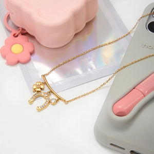 Detail of gold lucky necklace featuring horseshoe and flower pendants with white zircon
