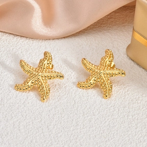 Detailed macro shot of gold starfish earrings with textured surface on silk background