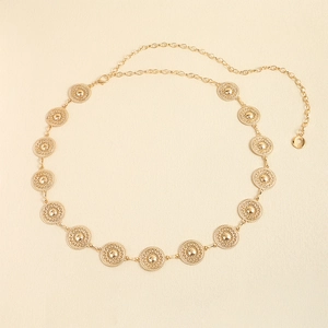 Detail of elegant gold chain belt featuring circular medal links on a beige background