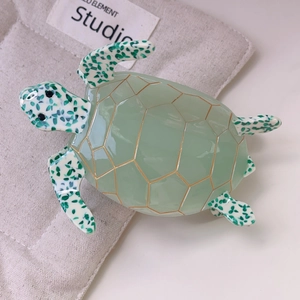 Detailed view of a green acetic acid sea turtle hair claw on a beige cotton pouch