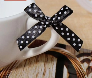 Close-up of black satin ribbon bow with white polka dots on a white ceramic mug handle