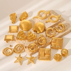 Close-up of heart, star, and geometric 18K gold earrings on textured beige stone base