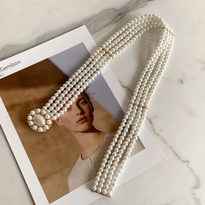 Detail of multi-layer white pearl waist chain with golden clasp on marble background