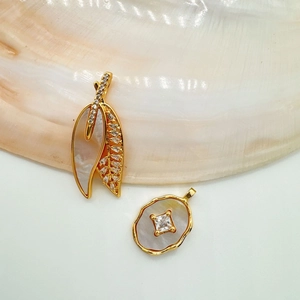 Detailed macro view of 18K gold-plated leaf and oval pendants with natural shells