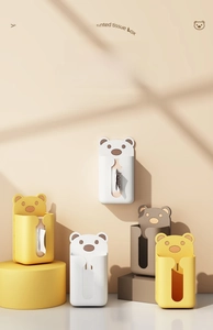 Three bear-shaped wall-mounted tissue boxes in white yellow and grey on display stands