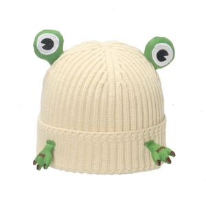 Detail of cream knit beanie showing green cartoon frog eyes and 3D stuffed hand accents