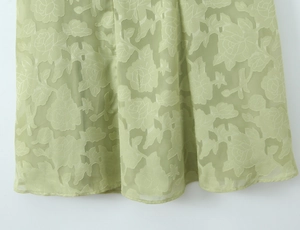 Detailaufnahme des hellgrünen floralen Jacquard-Stoffs und Saumstruktur des Kleides