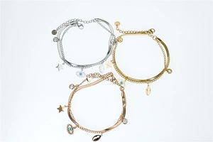 Close-up of evil eye, star, and shell charms on layered gold and silver snake bracelets