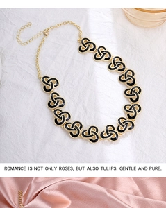 Gold chain necklace with black enamel clover links on white and pink silk fabric background