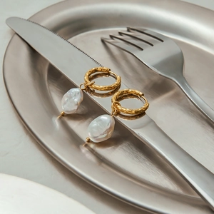Detail of gold hammered finish hoop earrings with white baroque pearls on metallic setup