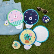 Outdoor layout of colorful folding fans and a matching tote bag on green grass