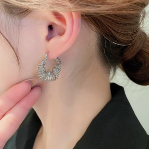 Close-up of woman wearing silver spiral coil hoop earrings with minimalist metal texture