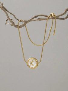 Detail of moon shell charm on gold snake chain hanging from minimalist branches