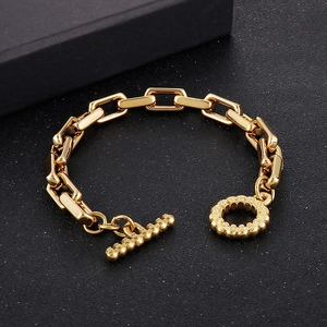 Gros plan d'un bracelet doré à maillons géométriques avec fermoir OT sur fond noir