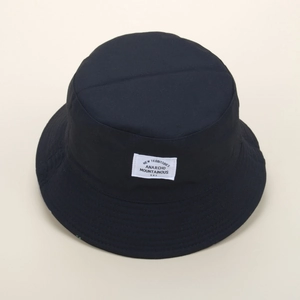 Detail view of the black cotton bucket hat featuring a white square woven patch label
