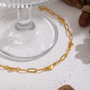 Polished 18K gold plated heart and link chain bracelet displayed on glass base