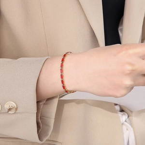 Close-up of gold chain bracelet featuring rectangular red zircons on a beige suit sleeve