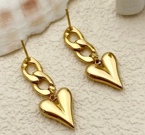 Close-up of golden stainless steel heart chain earrings on a white textured background
