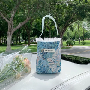 Close-up of teal fabric tote bag with leaf embroidery and white pleated trim in nature
