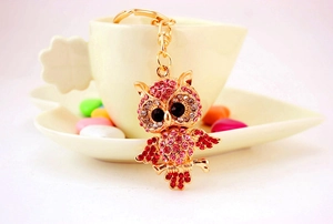 Close-up of gold owl keychain with pink rhinestones on a beige ceramic cup