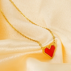 Detailed close-up of a gold heart pendant with red enamel inlay on silk fabric