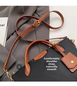 Detail of black nylon tote with brown leather trim and shiny gold metal hardware