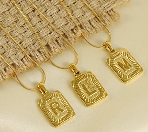 Détail de trois pendentifs lettres dorés rectangulaires sur des chaînes serpent
