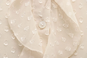 Macro shot of cream polka dot jacquard fabric with pearl button and ruffle detailing