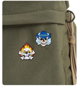 Macro shot of two punk skull enamel pins with flames and smoking hat on green canvas