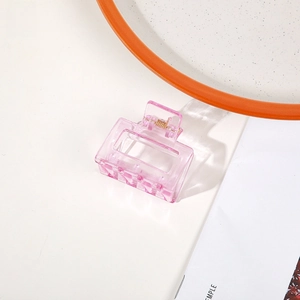 Close-up of a mini transparent pink rectangular claw clip with a gold metal spring