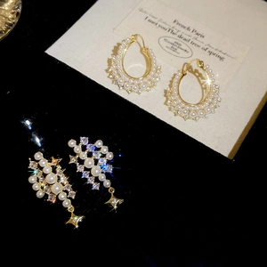 Detail of elegant gold pearl hoop earrings and star rhinestone drops on dark display