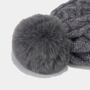 Close-up of a dark grey cable knit beanie featuring a fluffy faux fur pom-pom detail
