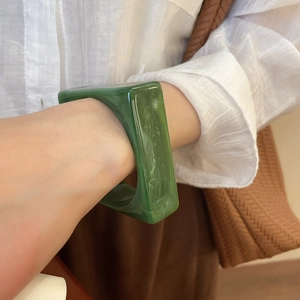 Detail of green acrylic rectangular bangle with marble texture worn by a model