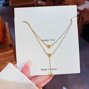 Double-layered gold necklace with spherical pendant shown on display card in detail