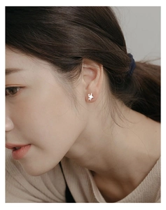 Macro shot of silver star-shaped stud earring worn by model showing small minimalist design