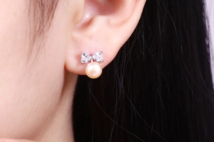Close-up of bow knot stud earring with heart zircons and light orange pearl on ear
