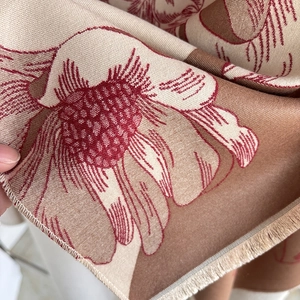 Detail of soft cashmere-like fabric with red floral magnolia patterns and tassels