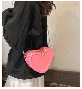 Rosa herzförmige Umhängetasche mit goldener Kette am Model für Outfit-Look