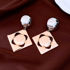 Detail of geometric earrings featuring gold square frames and silver semi-sphere studs